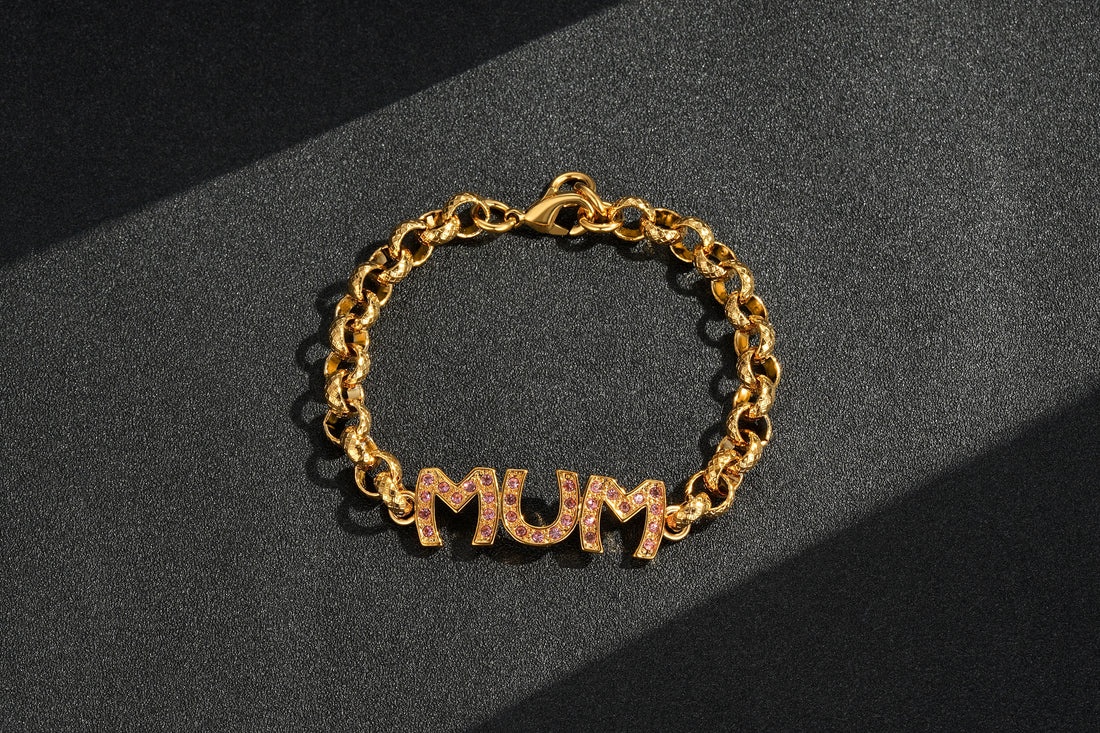 A gold mum belcher bracelet with pink stones, displayed on a dark surface.